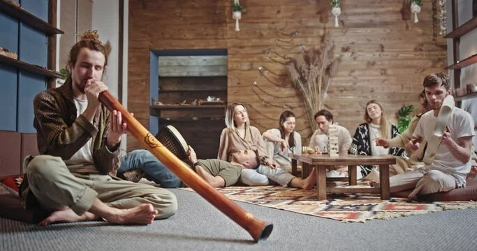 Hippies playing traditional musical instruments together. Group of friends playing authentic musical instruments and dancing while spitting on floor and chilling together in spacious room at home