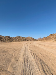 Fototapeta na wymiar Car tire tracks leading to small canyon with red sandstone rocks, Nabq protected area, Sharm El Sheikh, Sinai peninsula, Egypt, North Africa. Egyptian safari