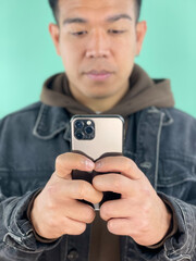 Handsome young asian man using a mobile phone, wearing casual clothes and green background. Active youth concept.