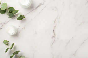 Skincare cosmetics concept. Top view photo of cream bottles and eucalyptus on white marble...