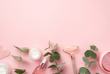 Skincare concept. Top view photo of rose quartz roller gua sha pink eye patches cream jars pink glass dropper bottle and eucalyptus on pastel pink background with blank space
