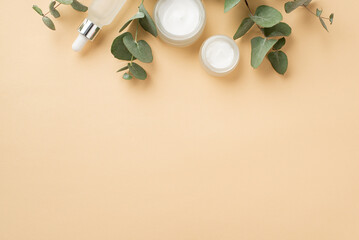 Skincare concept. Top view photo of glass dropper bottle cream jar and eucalyptus branches on isolated pastel beige background with blank space