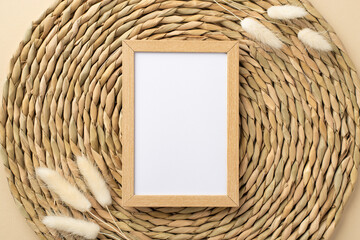 Top view photo of wooden photo frame and white lagurus flowers on decorative placemat with empty space
