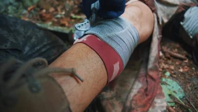 Close up combat medic with gloves give first aid to wounded soldier fix leg with a bandage. Military concept. Training