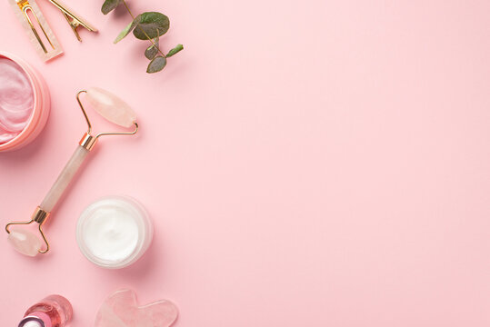 Skincare beauty concept. Top view photo of rose quartz roller gua sha pink eye patches cream jar glass bottle pink stylish barrettes and eucalyptus on pastel pink background with blank space
