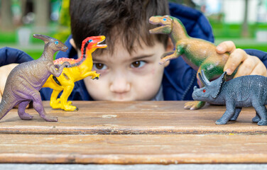 cute kid is playing with  dinosaurs toys on park bench, spring, green nature, grass. happy dinosaur...