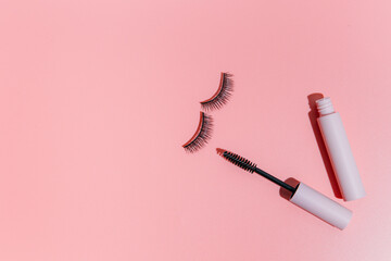 pink clear mascara brush lies next to the open tube and false lashes on a pink background, copy space. Makeup cosmetics set. Flat lay, top view.