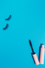 pink clear mascara brush lies next to an open tube and false lashes on a blue background, copy space. Makeup cosmetics set. Flat lay, top view.