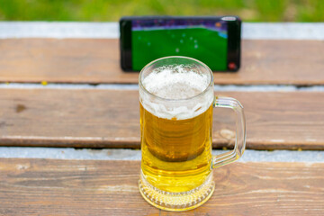 glass of beer on park bench in public park, green nature, spring, summer.
mobile phone,smartphone, with football match playing. world cup concept, football fans, on the go, big fan, idols.