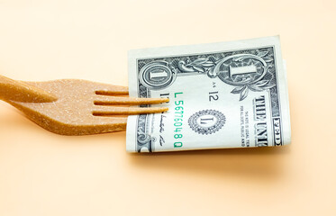 one dollar bill in the tines of a fork made from recycled materials on light orange background....