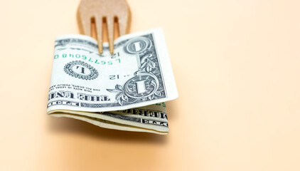 one dollar bill in the tines of a fork made from recycled materials on light orange background....