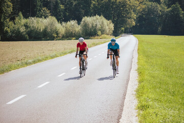Front view of a woman and man, professional racing bikers in sportswear, riding along an asphalt...