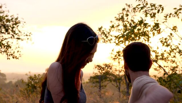 Happy love couple take photo and selfie during camping and relax in forest hiking trip, beautiful Asian woman and caucasian man happiness spend time tpgether, sunset liesure romantic moment