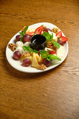 A plate with several varieties of cheese and fruit. Jam sauce in the middle of the plate