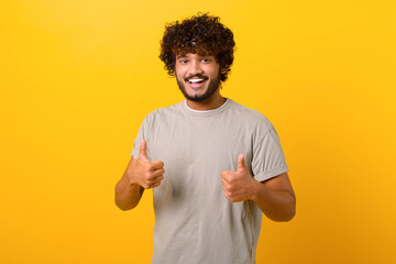 Like, excellent job. Pleased Indian man smiling to camera and gesturing thumbs up, approval hand...