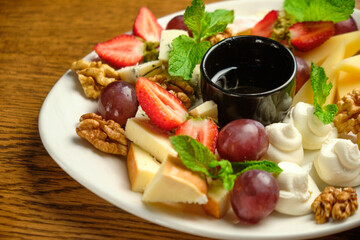 A plate with several varieties of cheese and fruit. Jam sauce in the middle of the plate