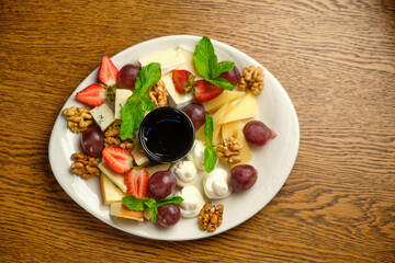 A plate with several varieties of cheese and fruit. Jam sauce in the middle of the plate
