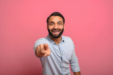 Joyful excited Indian middle-aged man in jeans shirt points fingers at the camera, surprised...