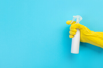 A hand in a yellow glove holds a white bottle of detergent on a blue background. Banner with copy space. Chemical cleaners, household chemicals, brushes and collage supplies. Cleaning concept.