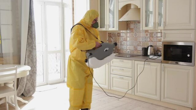 A man, an insect control specialist, in a yellow protective suit sprays the walls in the apartment, protects against viruses. Sanitary treatment