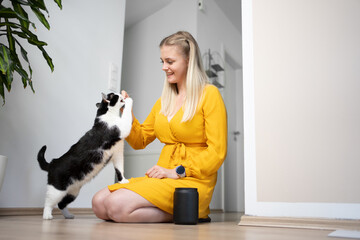 young blond woman with yellow dress kneeling on the floor  feeding snacks to her hungry cat