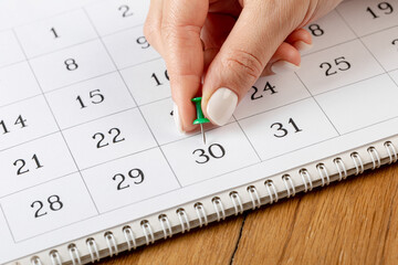 a female hand with a beautiful manicure holds a green pushpin to mark the date on the calendar 30 day