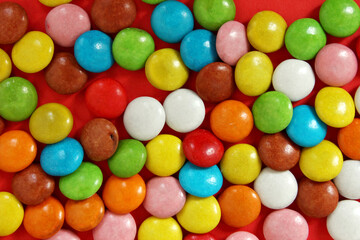 Fototapeta na wymiar Lots of colorful candy and chewing gum. colorful candy on a red background. Rainbow sprinkle for ice cream and cake. Small candies in colored chocolate glaze. background. Chocolate snack. Top view