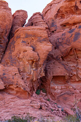 Overton, Nevada, USA - February 24, 2010: Valley of Fire. Closeup of cylindrical red rocks stacked against each other with caves, black spots and green shrubs in niches. Silver sky.