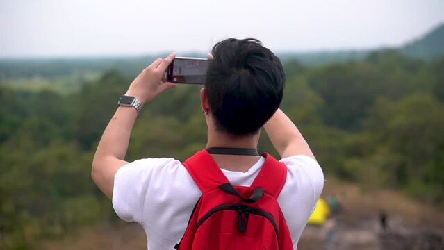 Young man tourist take photo on smartphone at mountain landscape view, stand shooting panorama on top hill. Male tourist traveling hiking outdoor alone with backpack in forest beautiful nature park. 