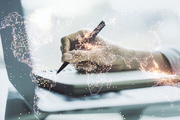 Multi exposure of abstract creative digital world map and hand writing in notebook on background with laptop, tourism and traveling concept