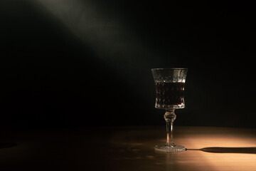 contrasting hard light with smoke illuminates a wine glass on a wooden table
