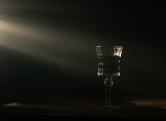 a crystal glass with wine in rays of light on a dark background with smoke