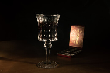 wine in a crystal glass with a reflection of a clock in a cosmetic bag on the table. dark background, general plan on a wooden table, vintage