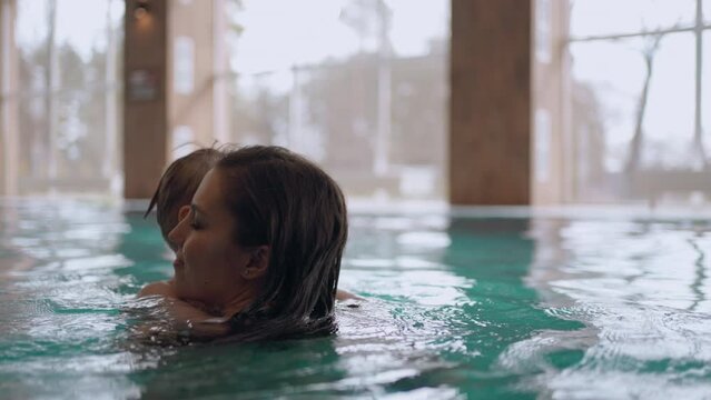 woman and her preschooler son are resting in water park, swimming in indoor pool