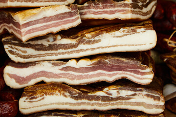 Smoked bacon is lined up on a market stall. You can see the fat layer of the meat. Pork.