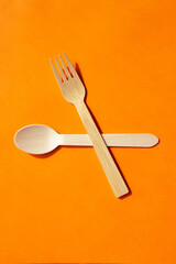 Wooden eco bamboo cutlery spoon and fork on bright orange background. Meal time concept
