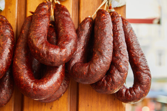 Red, smoked sausages hang in front of a wooden hingerund on a market stall. This kind of meat is very famous in Central Europe and Eastern Europe. Kolbasz