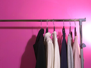 Clothes hung on a clothes rail wide shot pink background