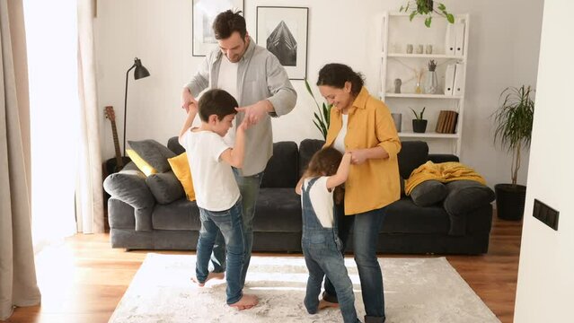 Overjoyed Cheerful Energetic Family Have A Fun In Cozy Living Room, Overjoyed Parents And Two Sibling Kids Fool Around, Dancing Weird Funny Dances