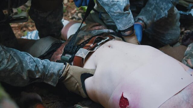 Close up combat medic applying tourniquet to wounded soldier. Getting ready to provide emergency medical treatment to injured soldier while danger military. In forest