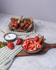 Schale mit geschnittenen Erdbeeren auf einem Brett und einer kleinen Schale Zucker, Korb mit...