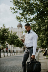 Young African American businessman using a mobile phone while waitng for a taxi on a street