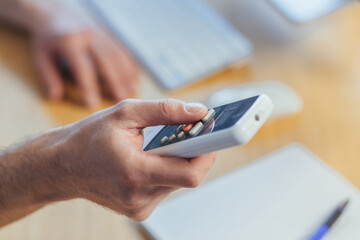 Close-up photo of a man's hand holding an air conditioner remote control, changing the temperature, businessman working in a bright office