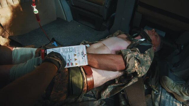 In car combat medic hold and read information about a wounded soldier. Receiving blood transfusion provides first aid. Military concept