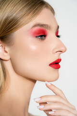 Young woman with red lips and eye shadow looking away isolated on grey.