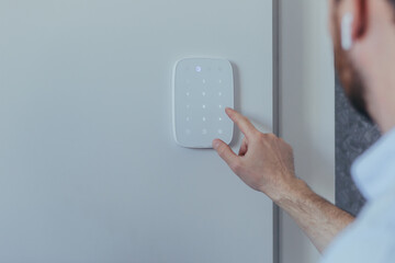 Businessman enters finger password lock code on alarm panel, on white wall, rear view of man with...