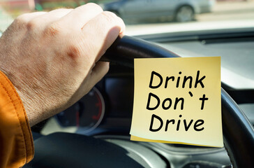 A man holds on to the steering wheel, next to a sticker with the inscription - Drink Do not Drive