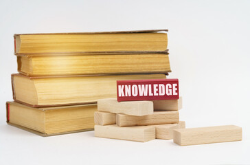 On a white surface, a stack of books and wooden blocks, on a red block there is an inscription - knowledge