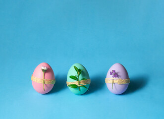 Colorful pastel eggs with spring flowers on light blue background. Creative Easter concept. Spring nature idea.
