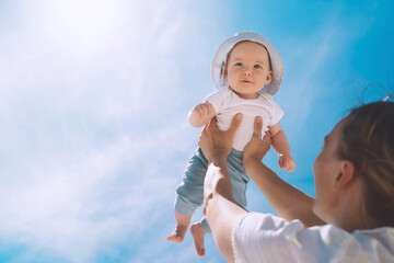 Mother throwing baby up against the blue sky. Happy family outdoors. Mom and baby at summer on nature. Positive human emotions and feelings.